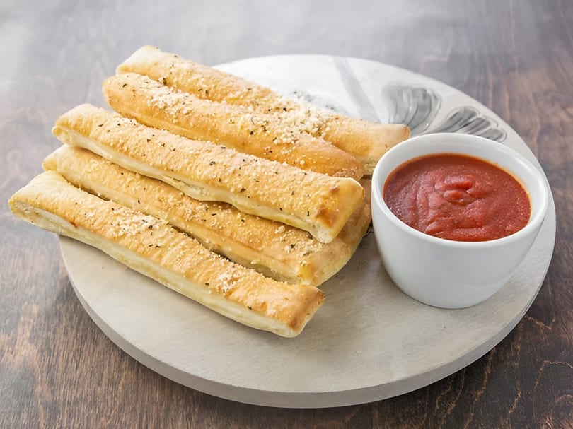 Golden-brown breadsticks sprinkled with parmesan cheese and herbs, served with a side of marinara sauce.