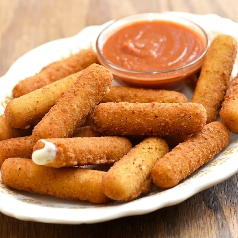 Golden-brown mozzarella sticks with a side of red marinara sauce on a white plate.