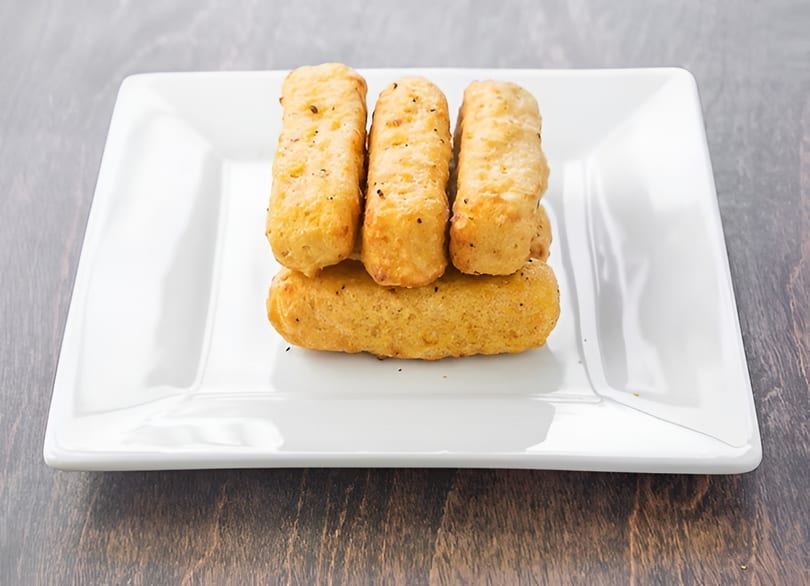 Five golden-brown mozzarella sticks, seasoned with herbs and spices, arranged on a white rectangular plate.