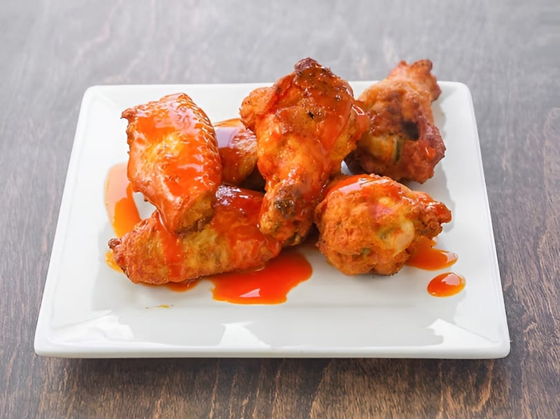 Crispy fried chicken wings coated in a vibrant orange buffalo sauce on a white rectangular plate.