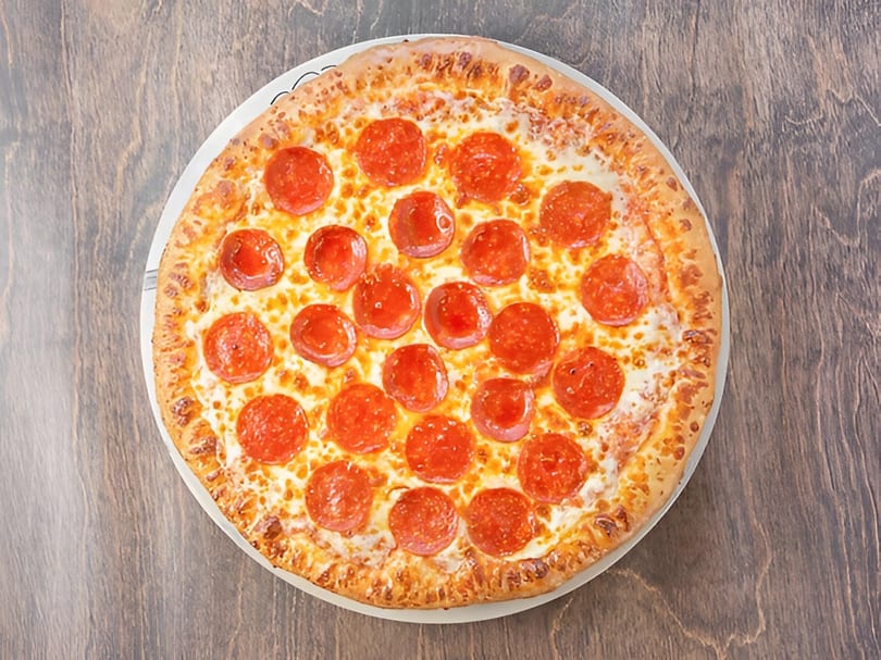 A whole pepperoni pizza with melted cheese on a white plate, viewed from directly above.