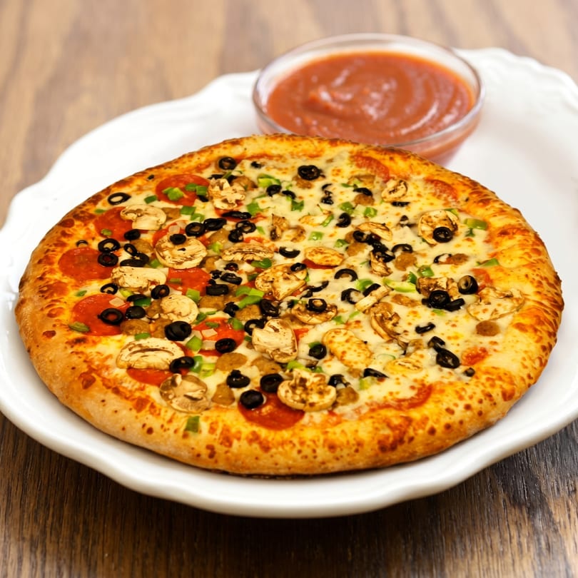 A whole pizza with pepperoni, mushrooms, olives, and green peppers, served with a side of sauce.
