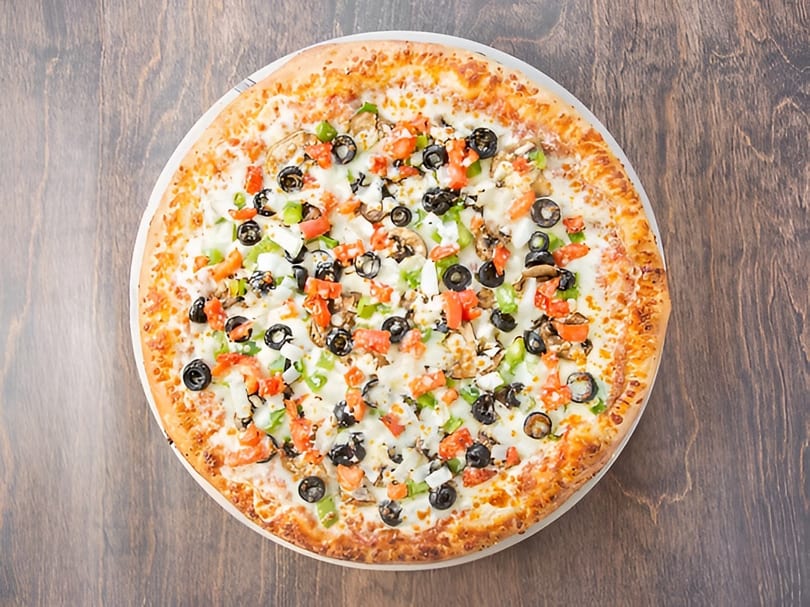 A whole vegetarian pizza with olives, peppers, tomatoes, and mushrooms on a wooden table.
