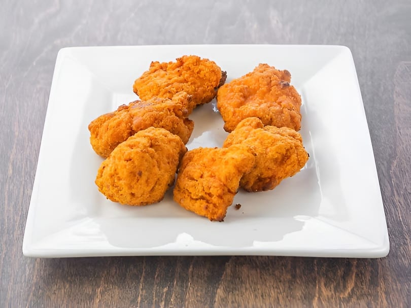 Seven crispy, golden-brown fried chicken nuggets arranged on a white square plate.